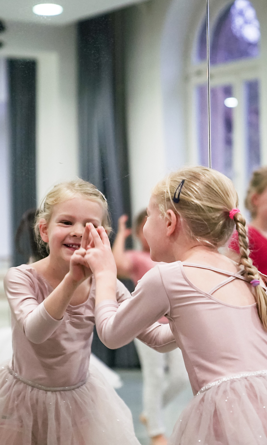 Mädchen im Tutu zeigt auf ihr Spiegelbild.