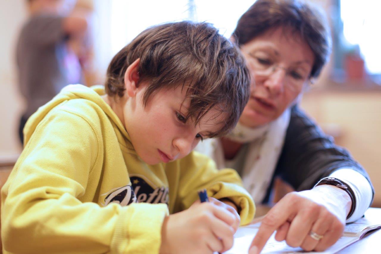 Kind schreibt, Lehrerin unterstützt
