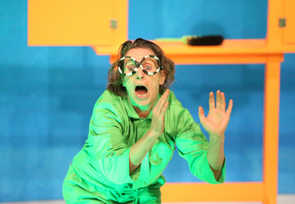 Frau hat eine Zebra-Brille auf und hat einen grünen Overall an. Sie schaut erschrocken.