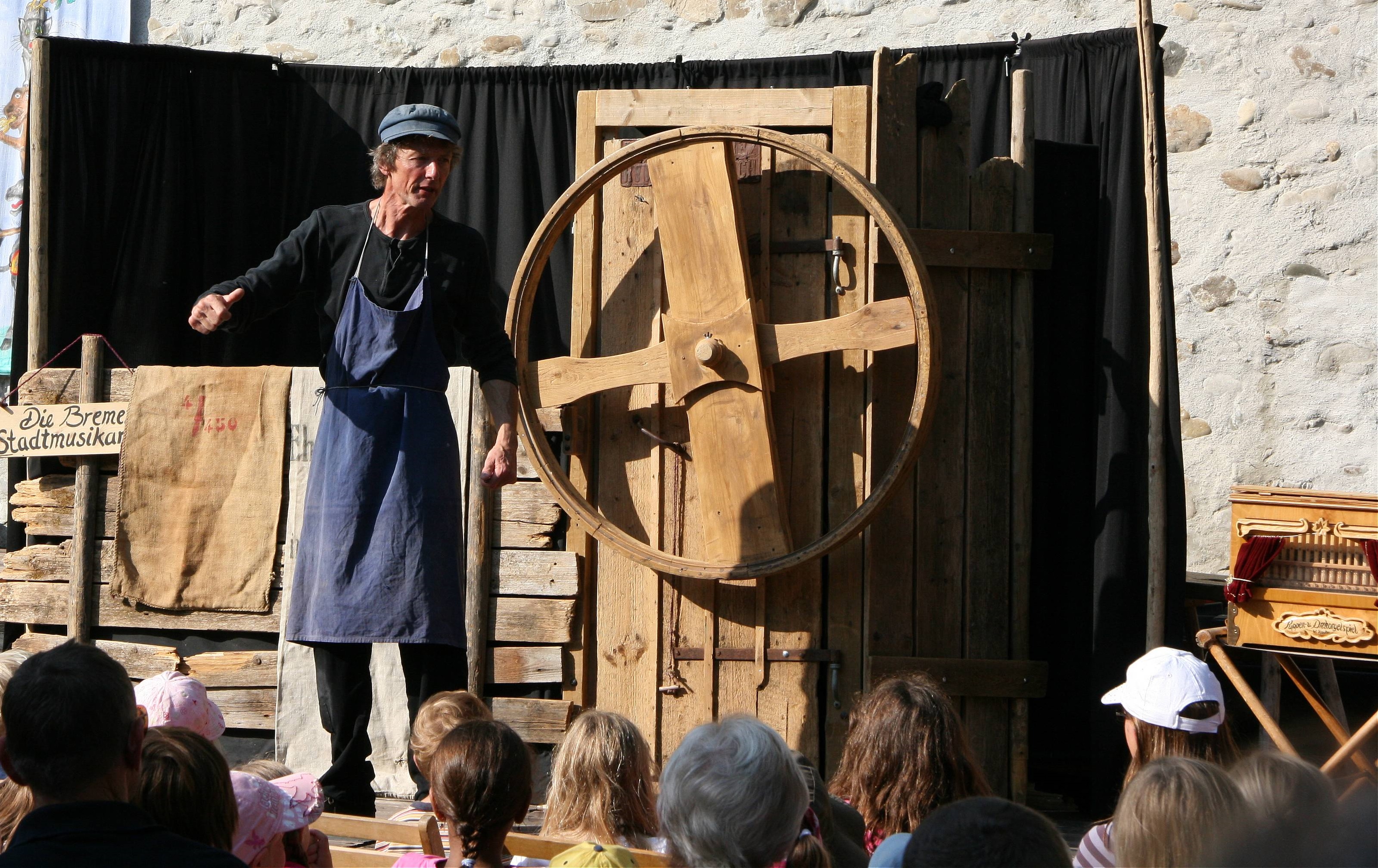 Mann steht als Müller verkleidet auf einer Bühne neben einem Mühlrad.