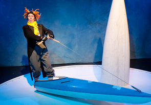 Frau als Pinguin verkleidet, steht auf einer Art Surfbrett.