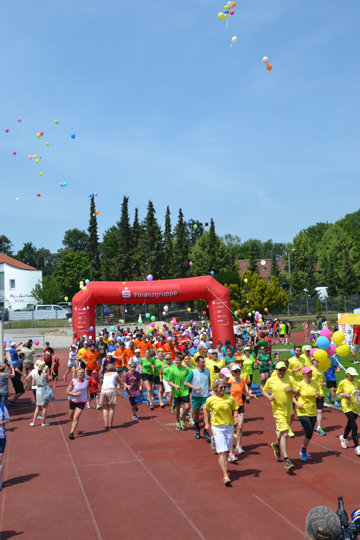 Start zum 24 Stundelauf auf einer Tartanbahn. Im Hintergrund steigen viele Luftballons auf.