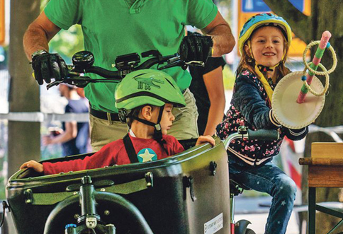 Vater sitzt auf einem Fahrrad. Vorne in einem großen Korb sitzt ein Kind.