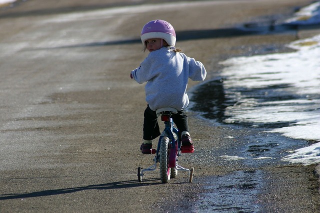 Mädchen sitzt auf einen Fahrrad mit Stützrädern und schaut über die linke Schulter nach hinten.