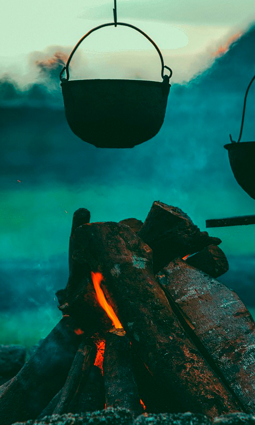 Zwei eiserne Töpfe hängen über einer Feuerstelle.