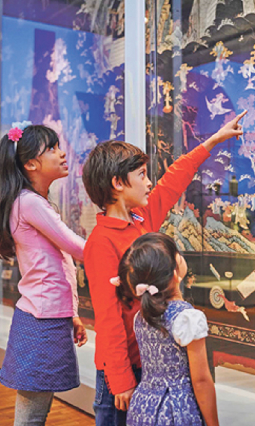 Drei Kinder stehen vor einem Schaukasten im Museum. Der Junge zeigt mit dem Finger auf etwas.