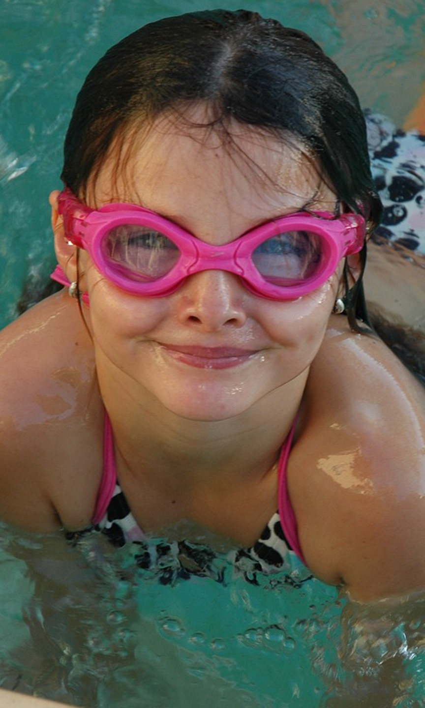 Mädchen schwimmt im Wasser. Es trägt eine pinke Taucherbrille.