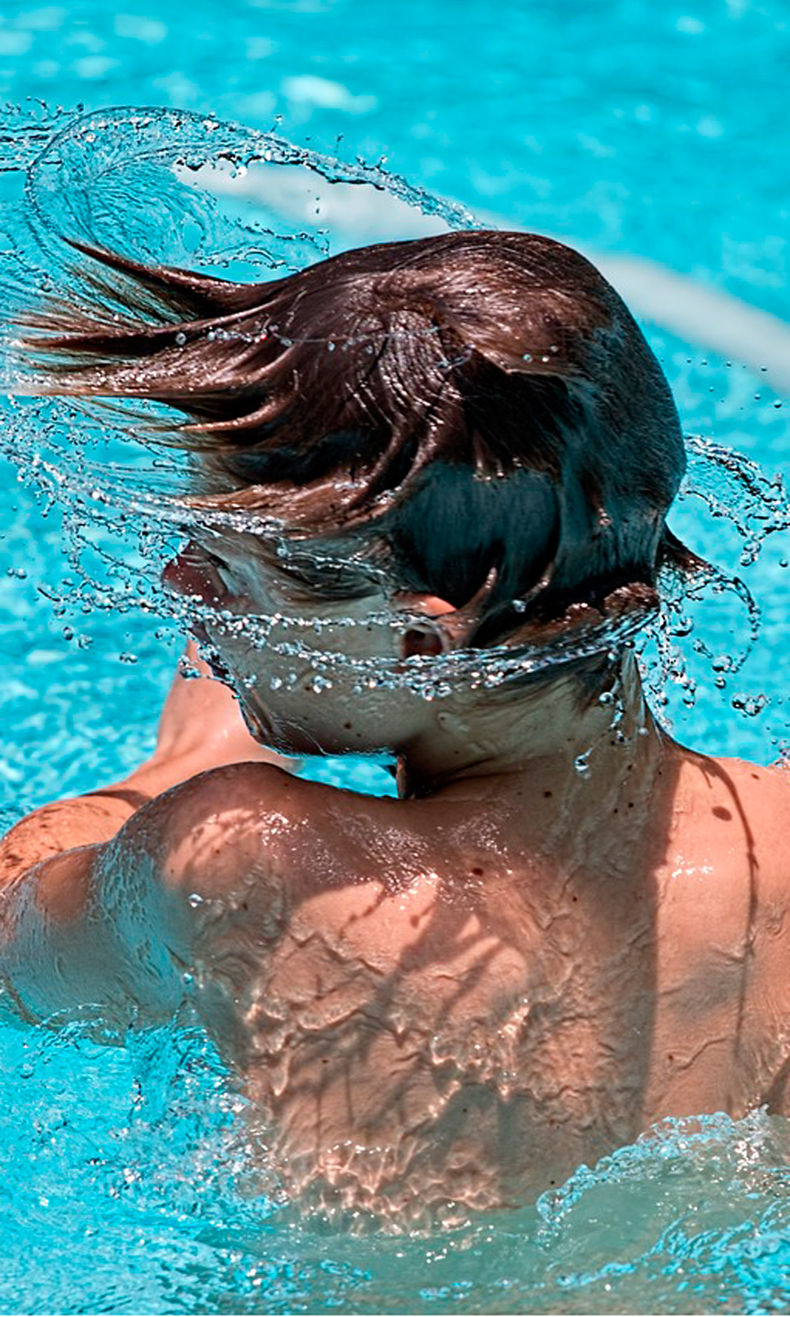 Junge ist aus dem Wasser aufgetaucht und schüttelt sich das Wasser aus den Haaren.