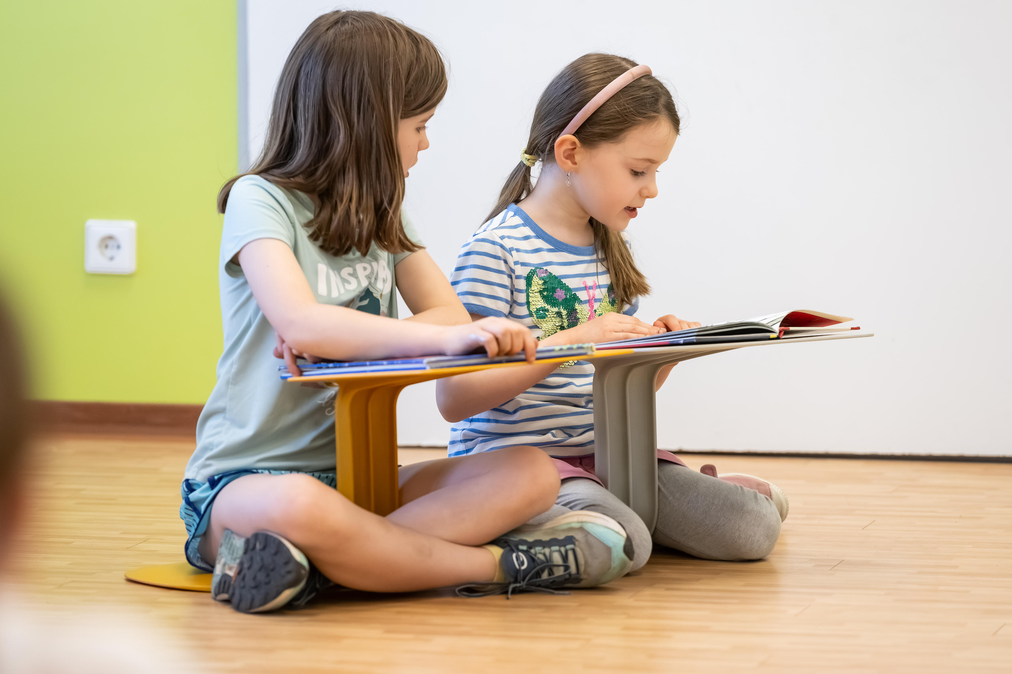 Zwei Mädchen beim Lesen am Schribpult im Schneidersitz
