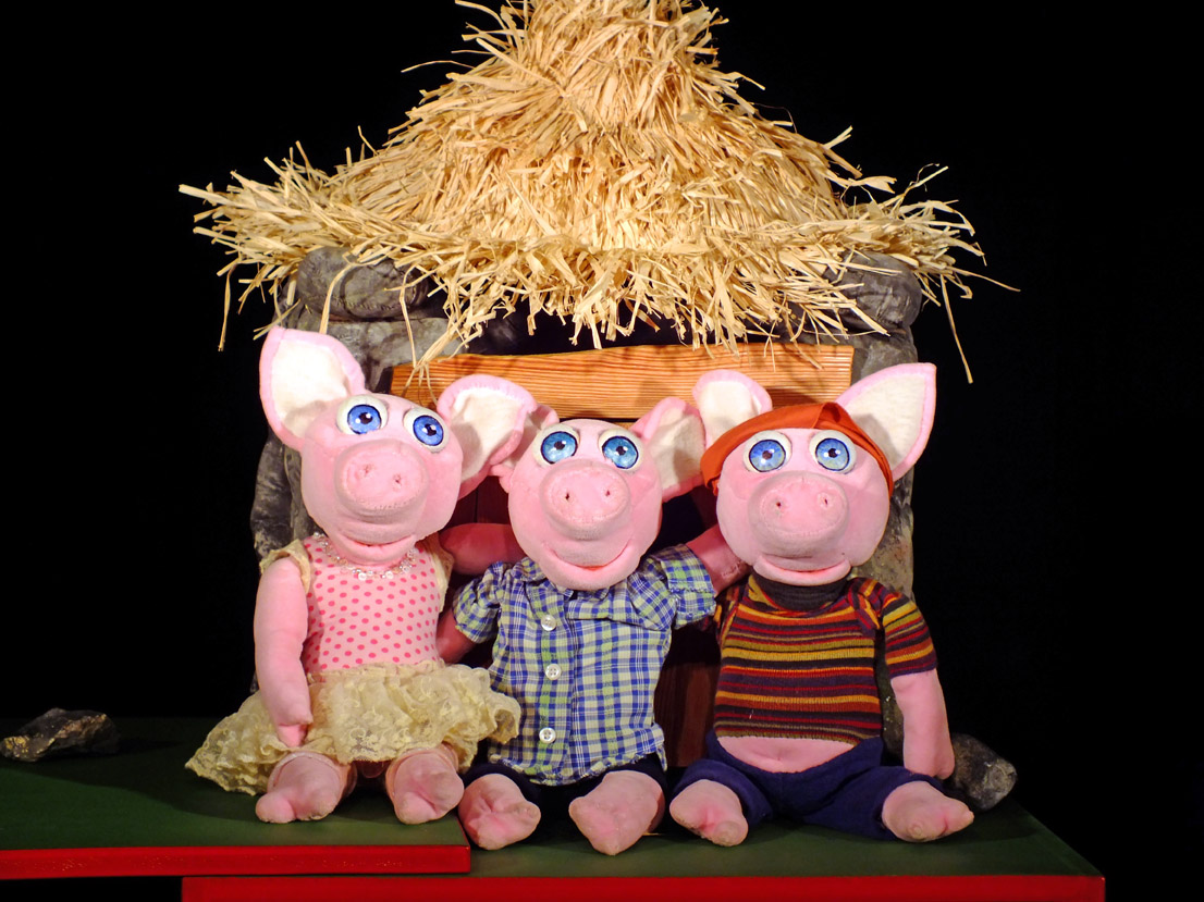 Drei kleine Schweinchen sitzen vor einem Stall