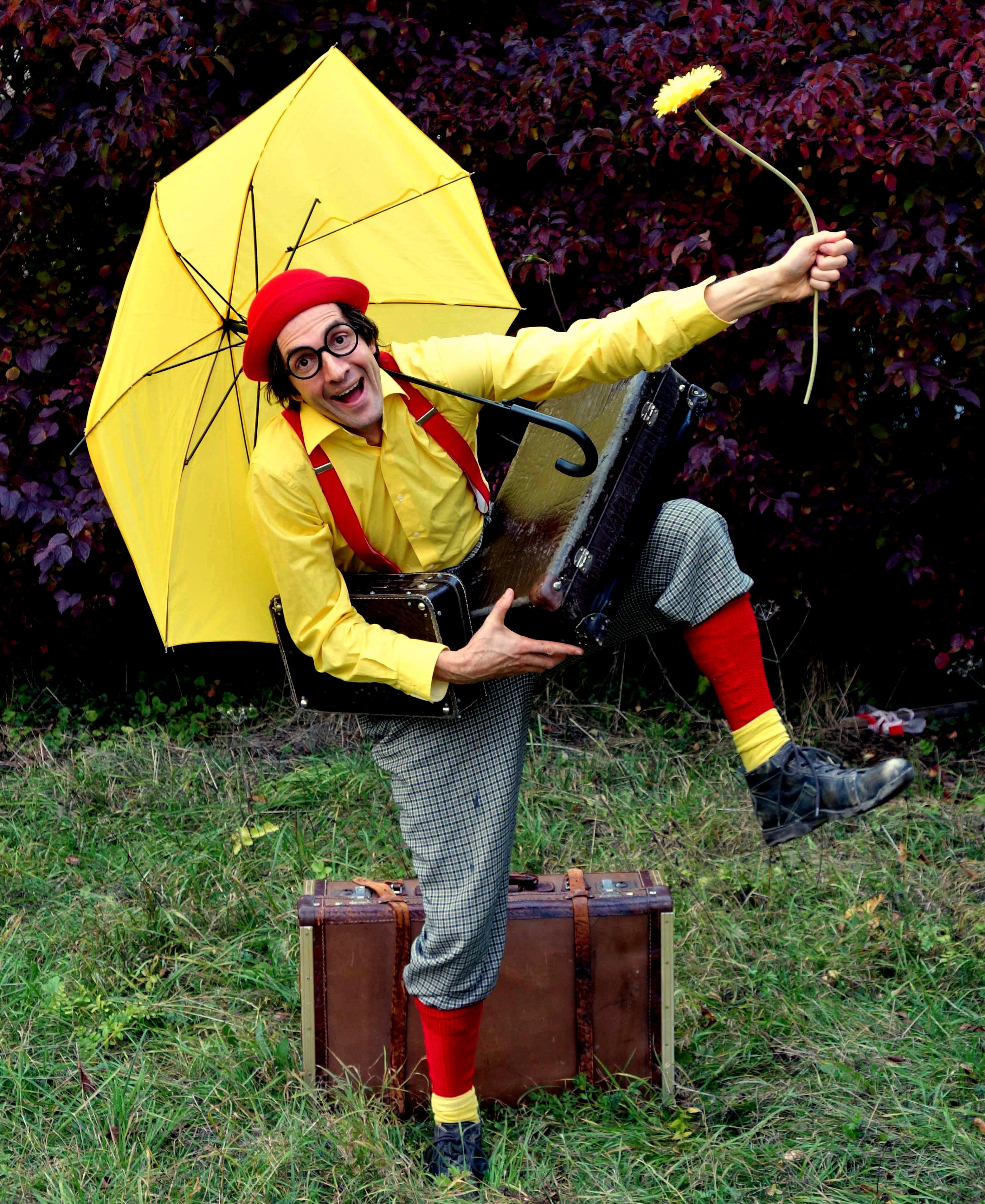 Mann in einem bunten Clownskostüm mit einem gelben Regenschirm.
