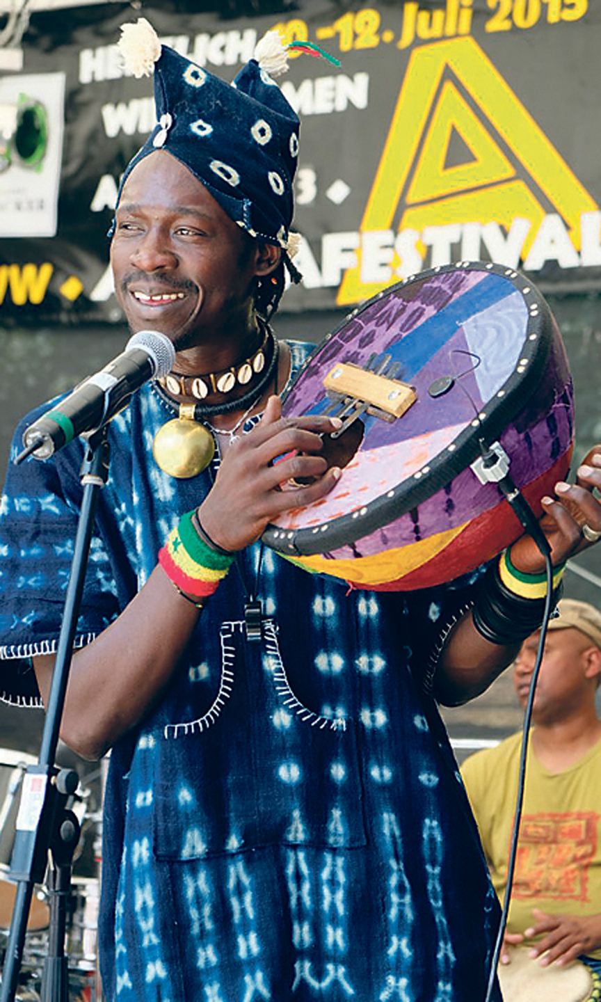 Mann mit traditioneller, afrikanischer Kleidung spielt auf einer Trommel und singt.