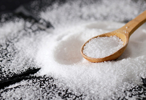 Ein Häufchen Salz liegt auf einen Tisch. Ein Holzlöffel liegt darin.