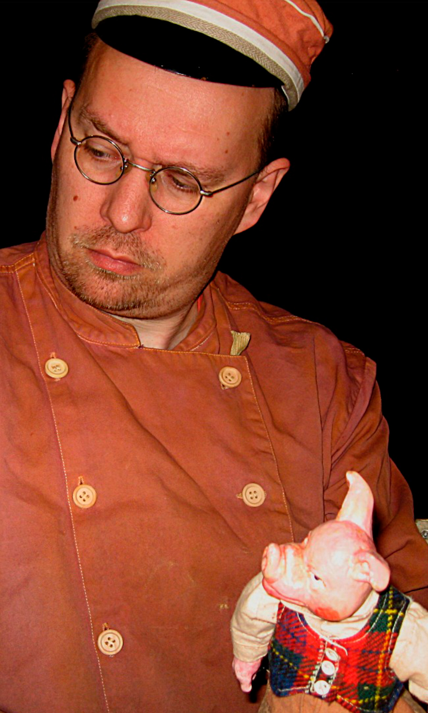 Handpuppenspieler, der eine Zugschaffner-Uniform trägt und eine Schweine-Handpuppe in der Hand hält.