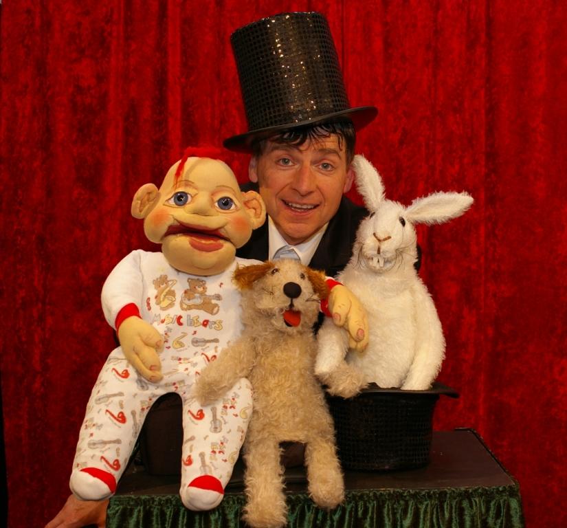 Mann mit Zylinder und 3 Puppentheater-Figuren.