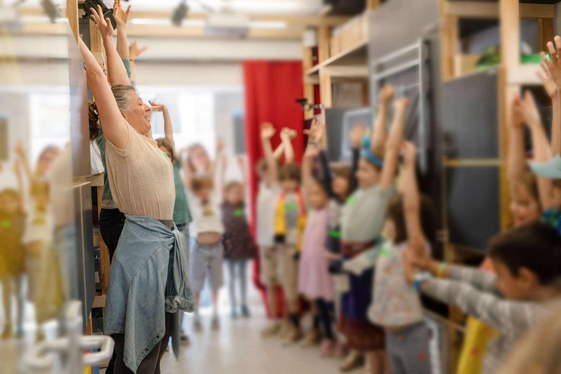 Eine Frau streckt die Hände in die Luft. Viele Kinder machen es ihr nach.