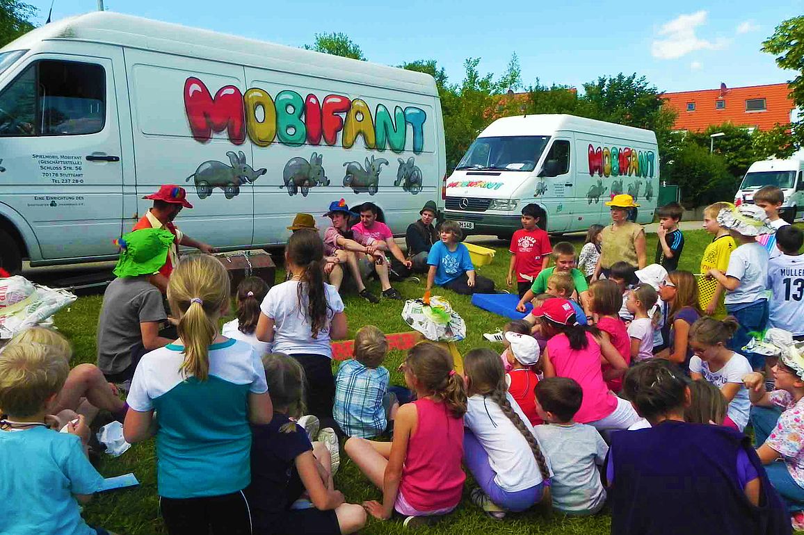 Kinder sitzen vor dem Wagen des Spielmobils.