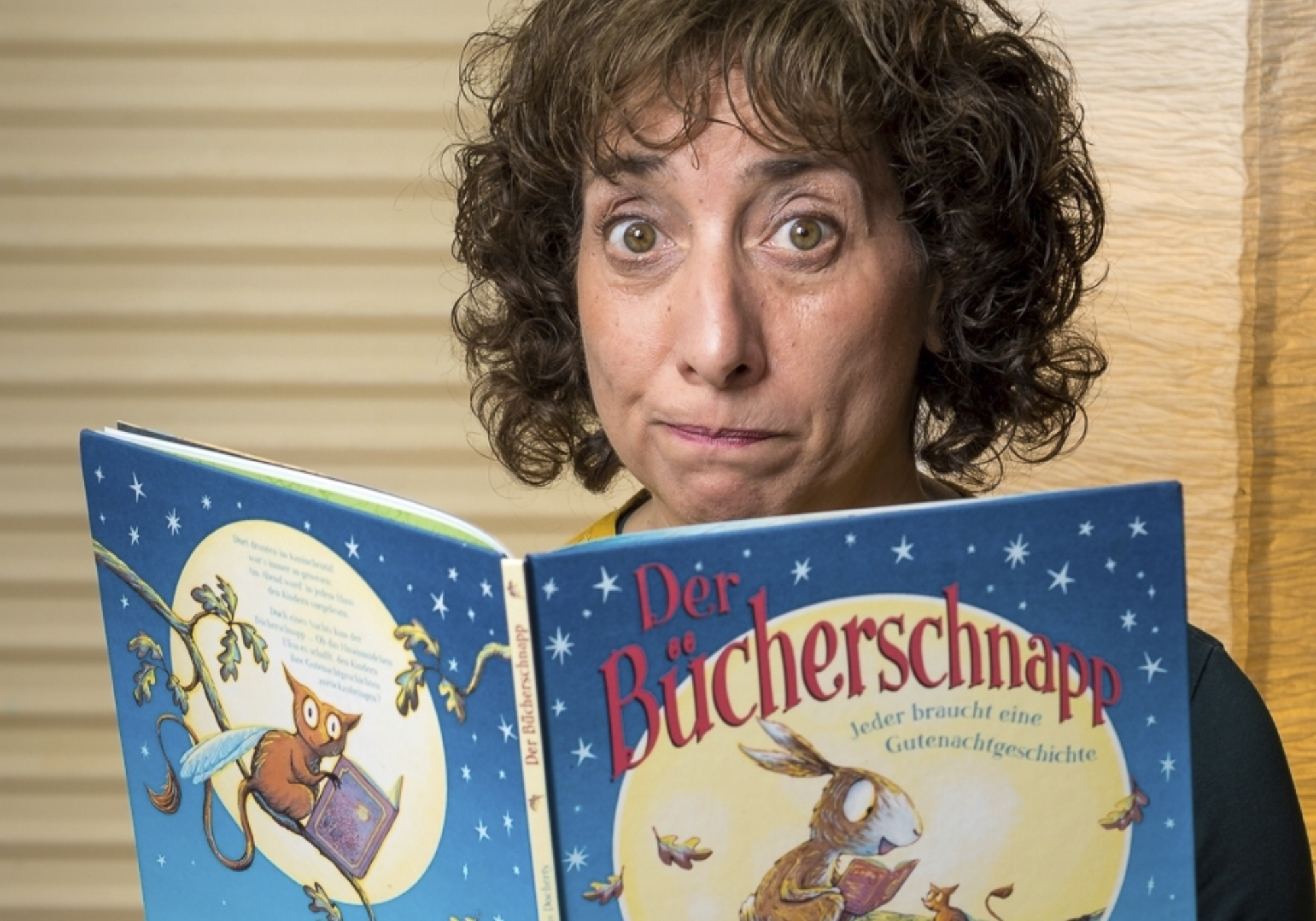 Frau schaut über den Rand eines Buches in die Kamera.