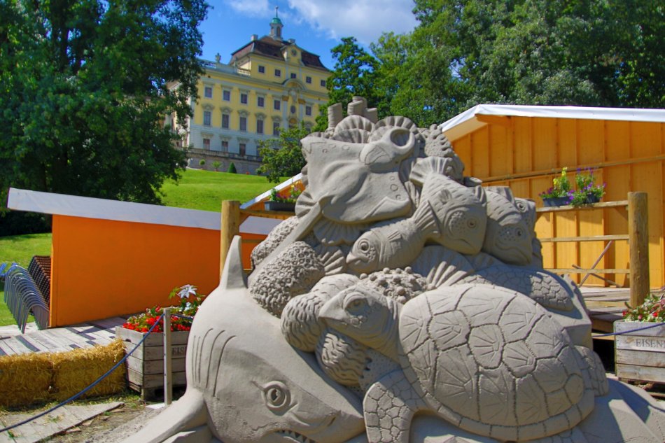 Im Hintergrund das Ludwigsburger Schloss. Im Vordergrund eine Figur aus Sand.