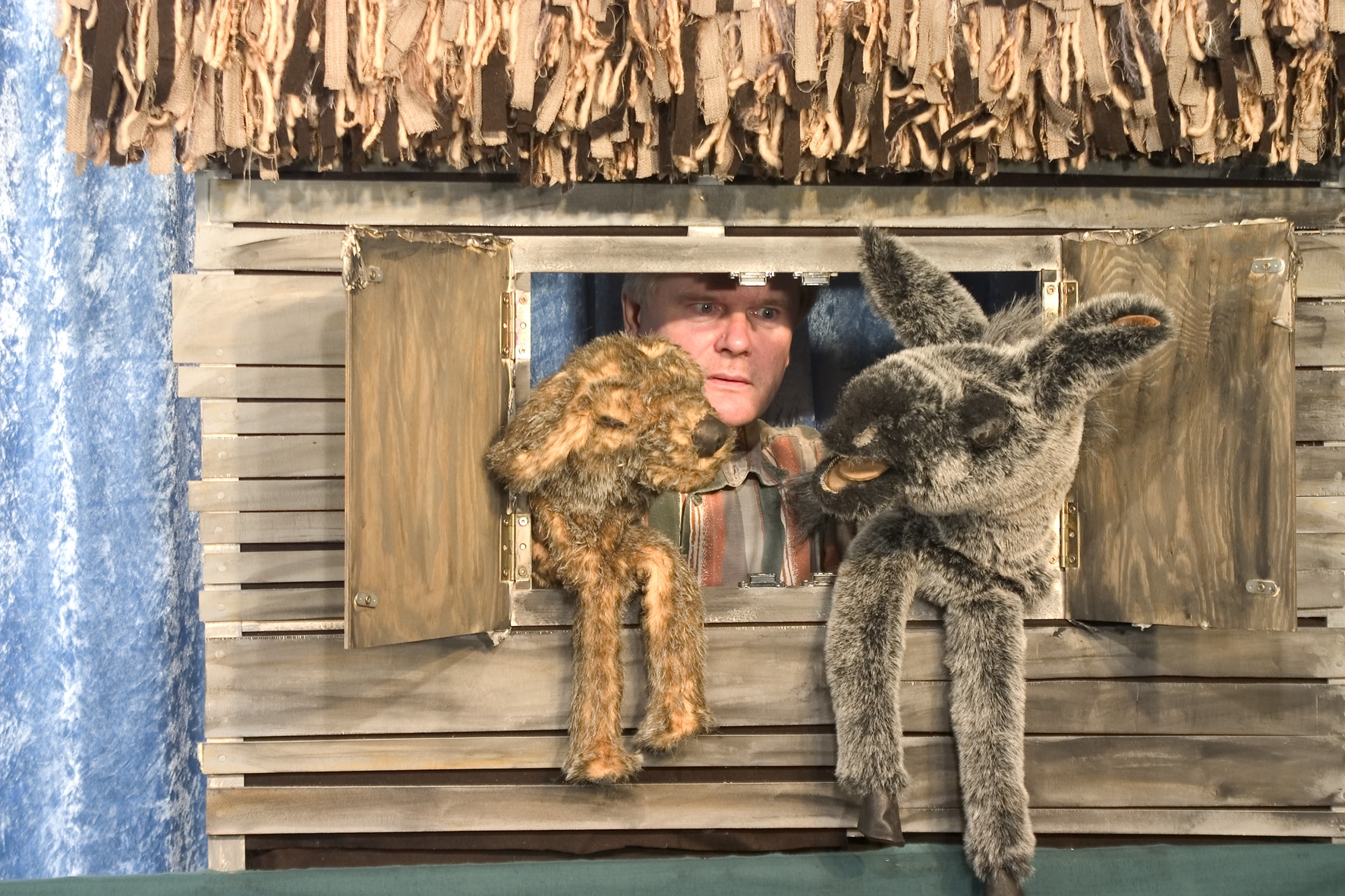 Esel, Hund, Katze, und Hahn schauen aus einem Fenster ins Freie. Im Hintergrund der Puppenspieler