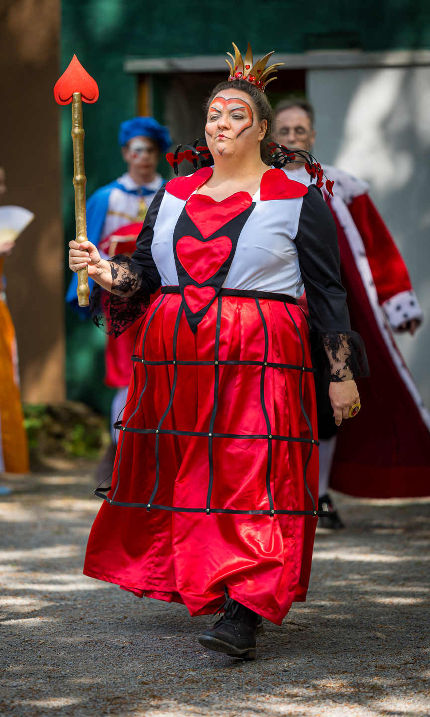 Man sieht eine Schauspielerin auf einer Bühne, die als die Herz-Königin aus Alice verkleidet ist.