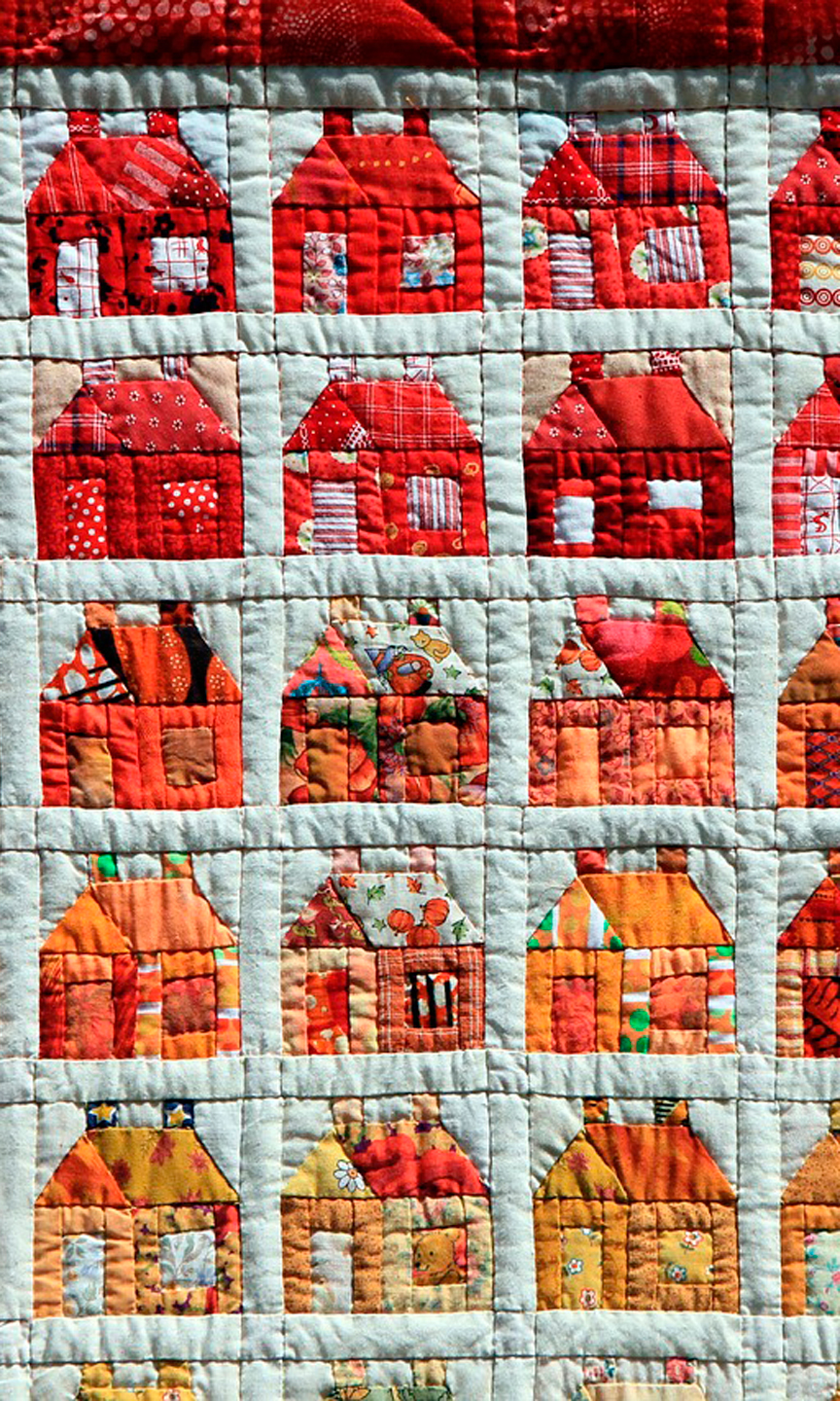 Patchworkdecke auf der viele unterschiedlich rote und organgene Häuser zu sehen sind.