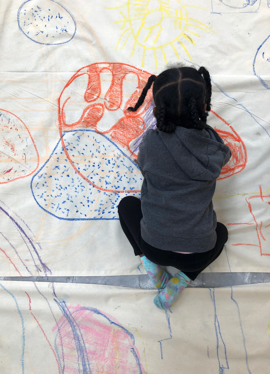 Kind, das auf einem griooßen Papier knied und eine Landschaft zeichnet