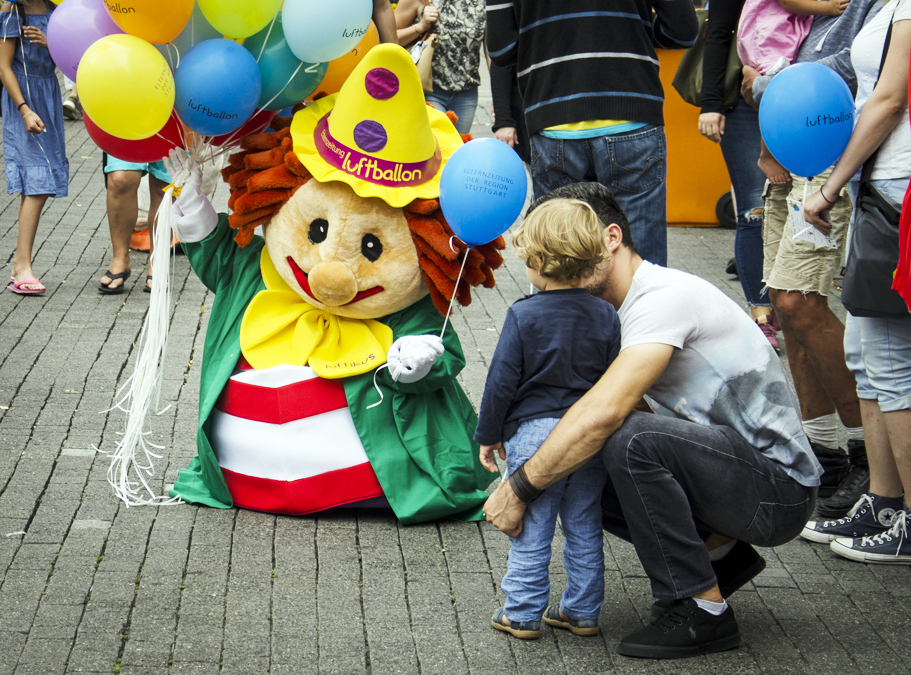 Die Clownsfigur Luftikus winkt in einer Gruppe von Menschen