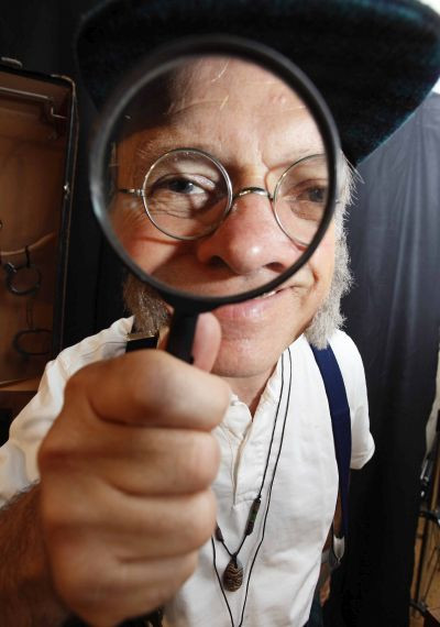 Alter Mann schaut durch eine Lupe in die Kamera.