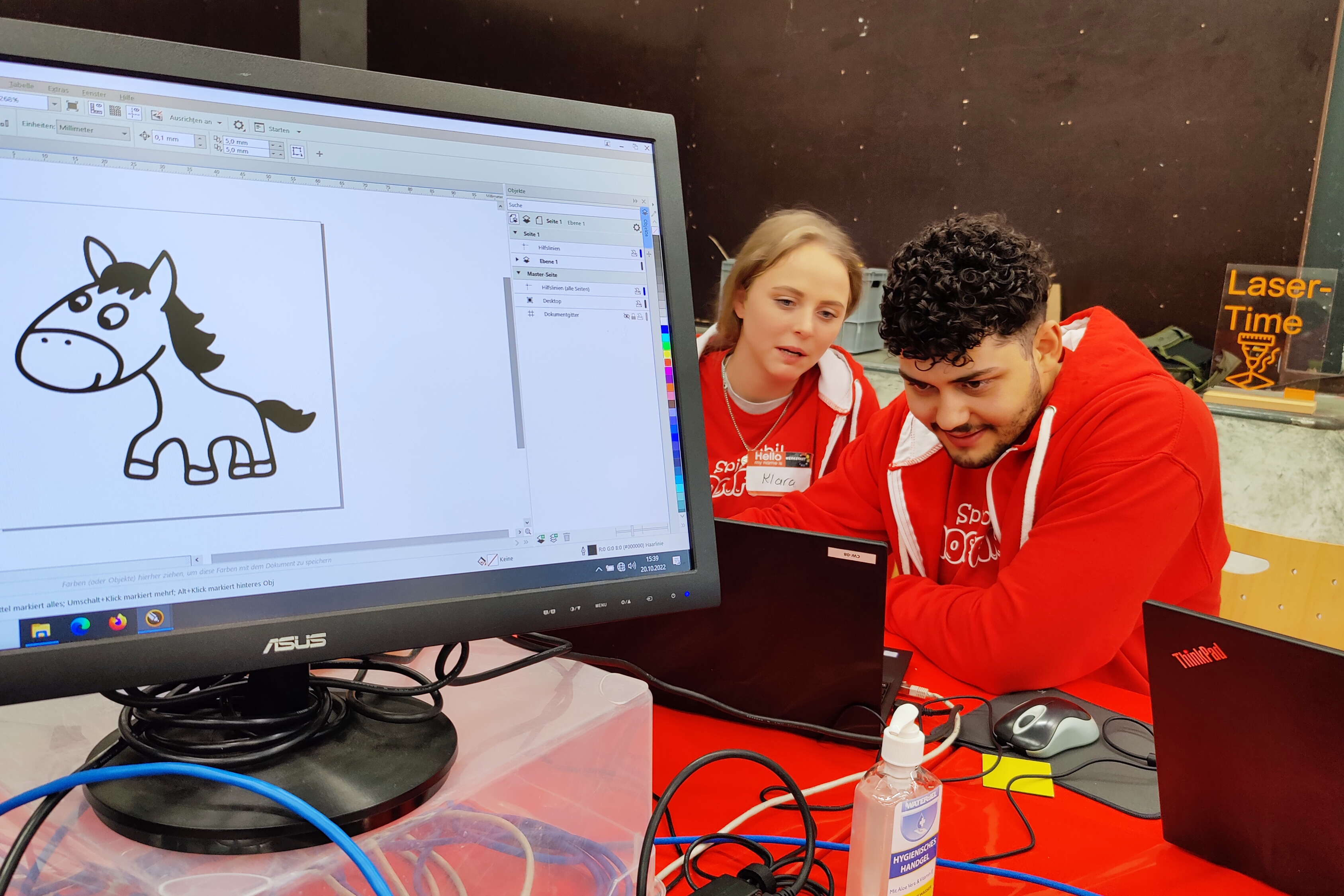 Im Vordergrund ein PC-Monitor, im Hintergrund zwei Kinder beim tüfteln.