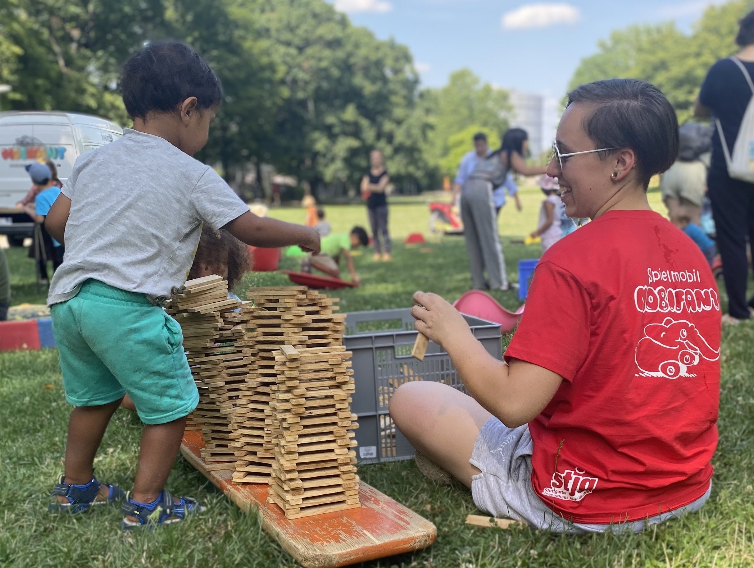 Ein kleiner Junge stapelt einen Turm, eine Frau vom Spielmobil schaut zu.