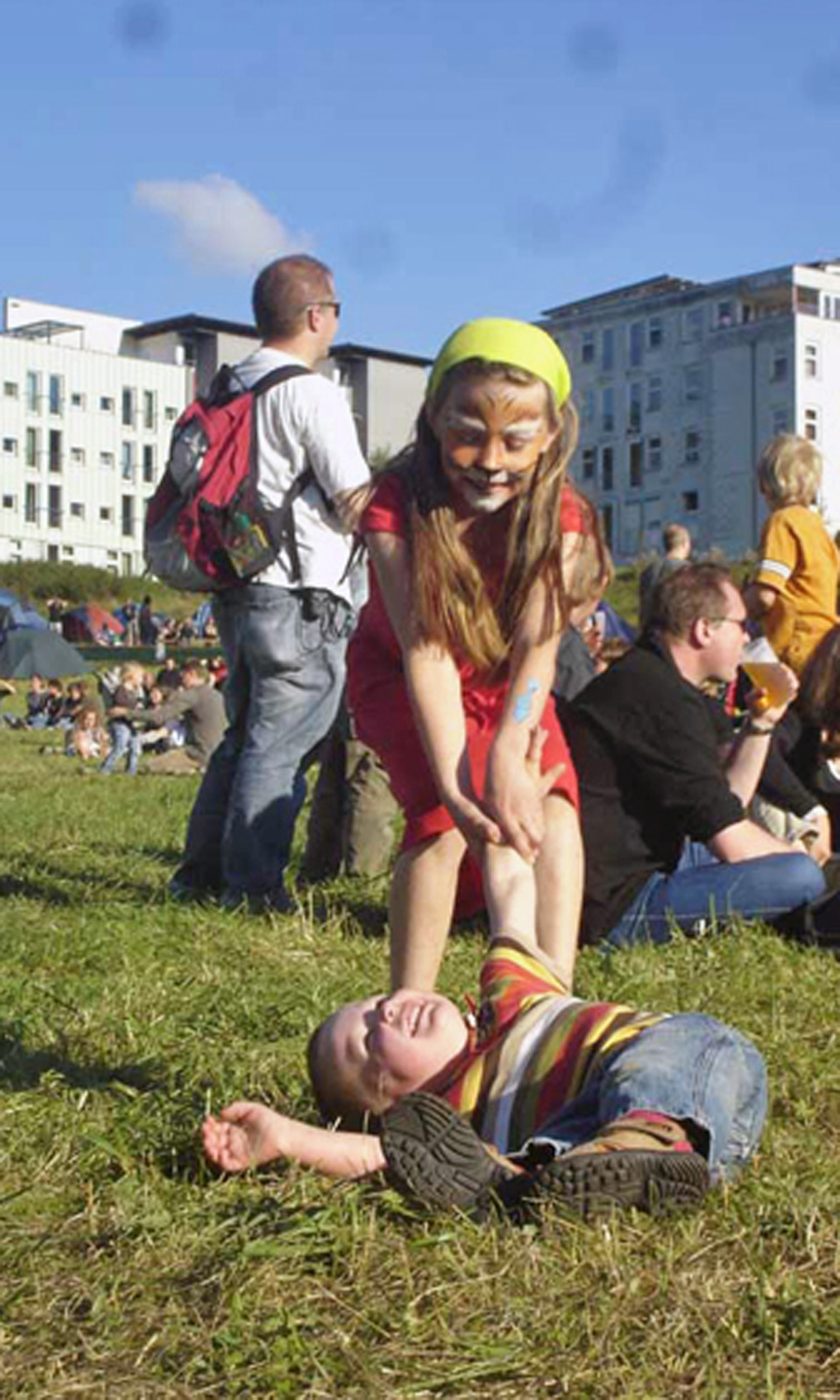 Im Hintergrund sieht man Mehrfamilienhäuser. Im Vordergrund sitzen Familien auf einer Wiese.