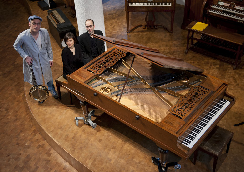 Drei Menschen stehen um ein großes Klavier herum.