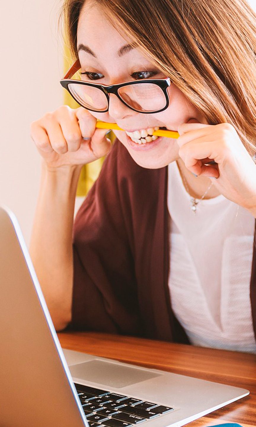 Frau sitzt vor einem Computer und beißt in einem Bleistift.