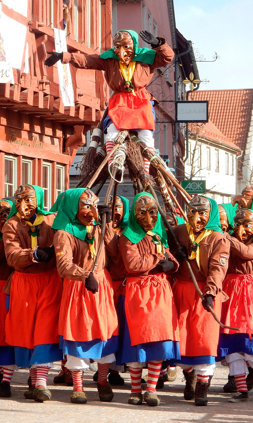 Faschingsumzug. Eine Narrengruppe aus Hexen baut eine menschliche Pyramide.
