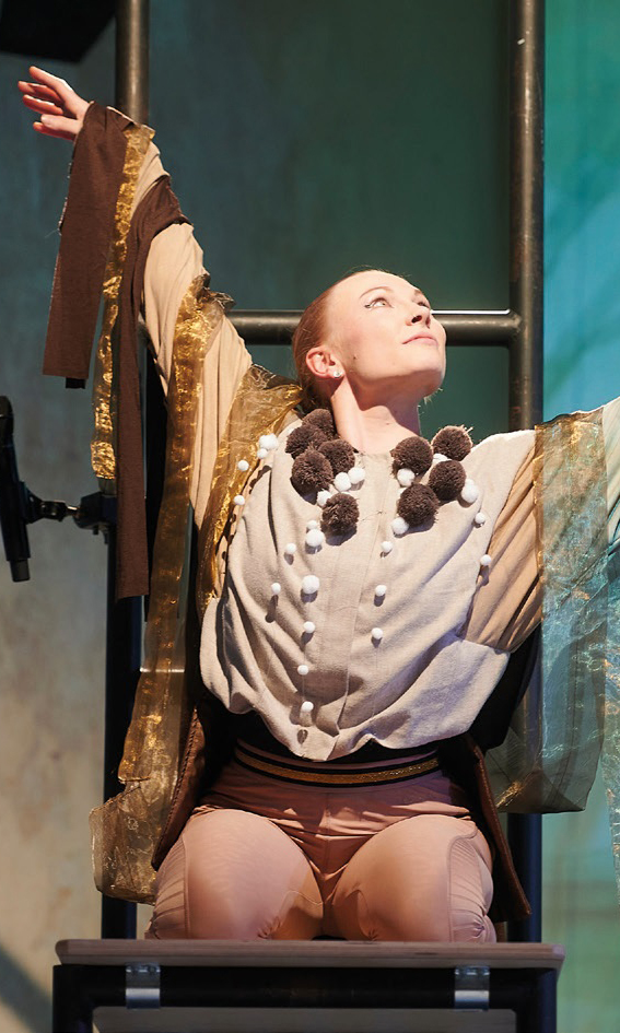 Eine Tänzerin mit Bändern um die Arme streckt diese in die Höhe.