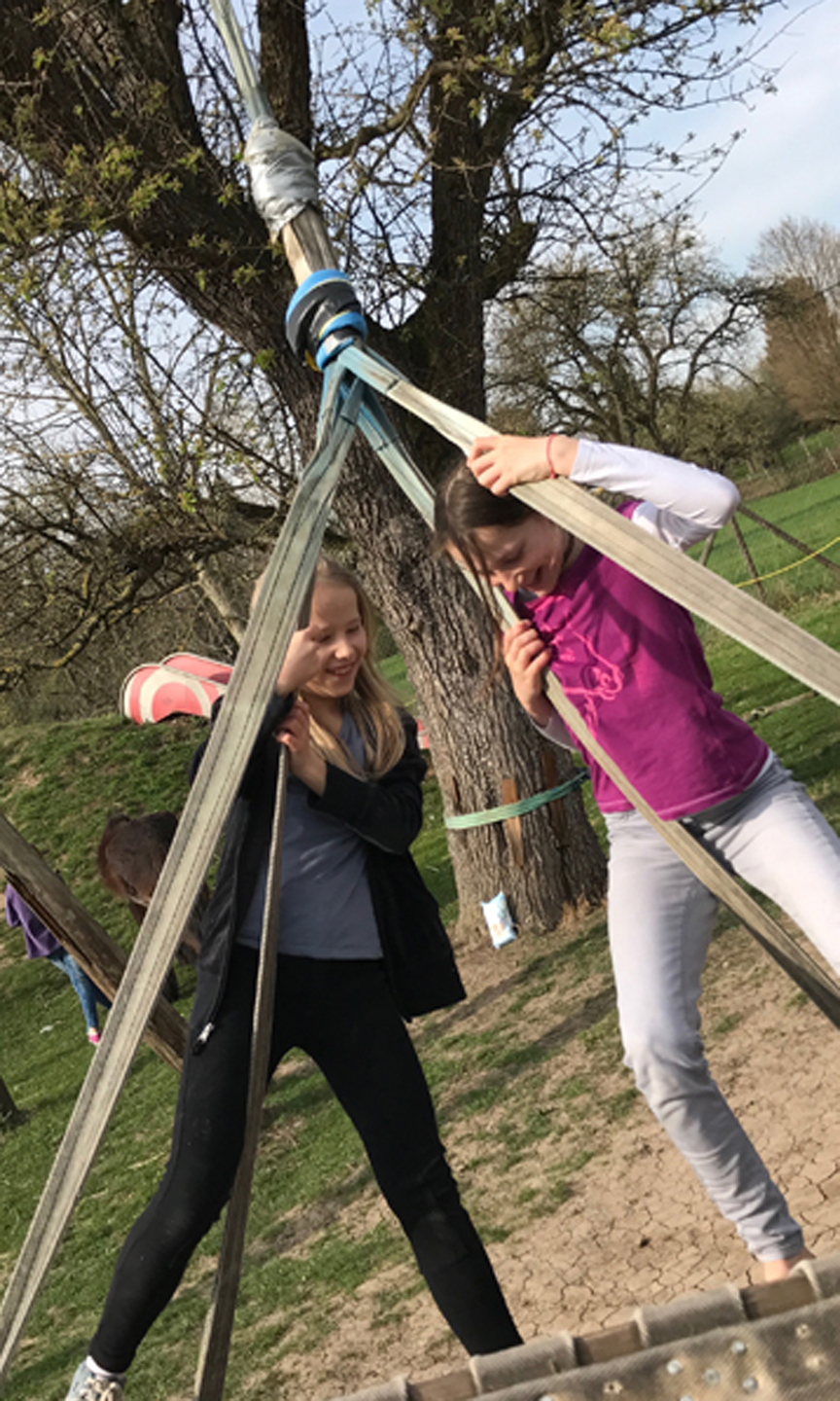 Zwei Mädchen klettern auf einem Holzspielgerät.