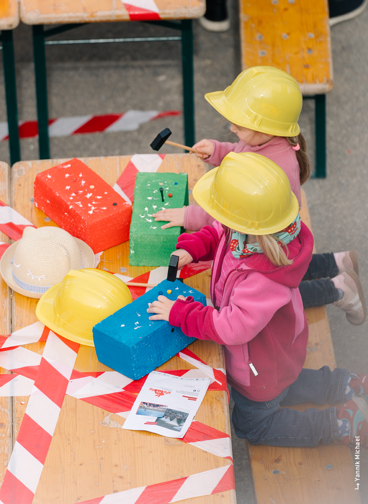 Kinder in Bauklamotten sitzen an einem Tisch mit großen Bauklötzen.