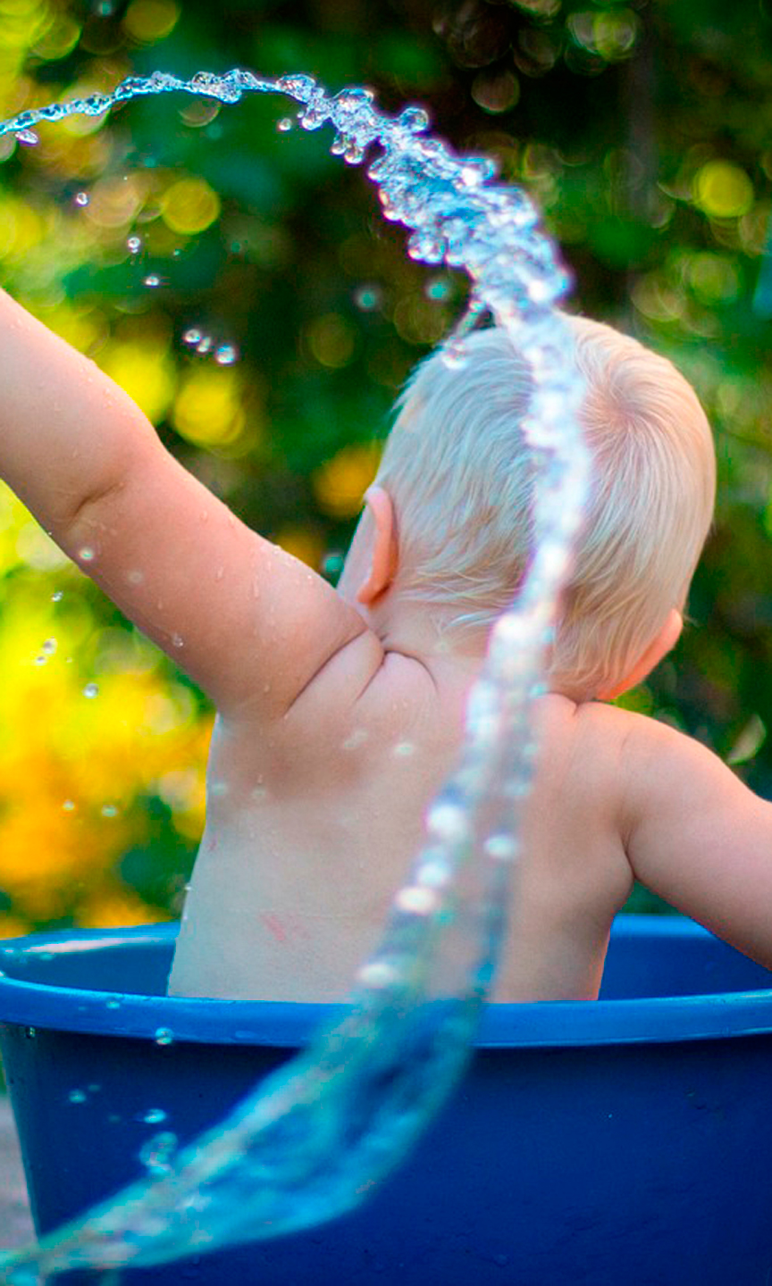 Kleinkind sitzt in einem großen Eimer und spielt mit Wasser.