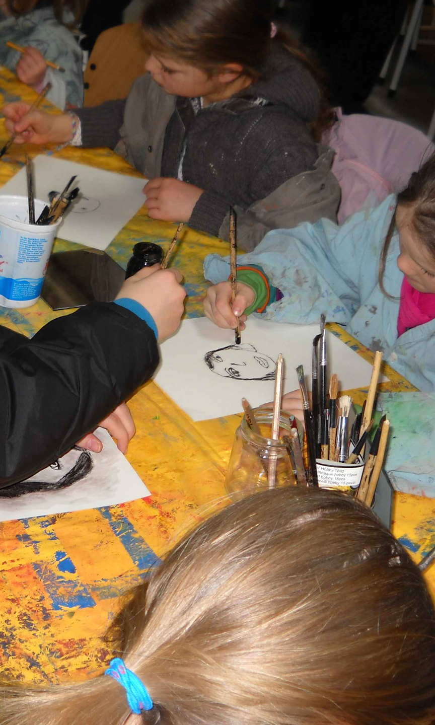 Kinder sitzen gemeinsam am Tisch und malen mit Farbe und Pinsel.