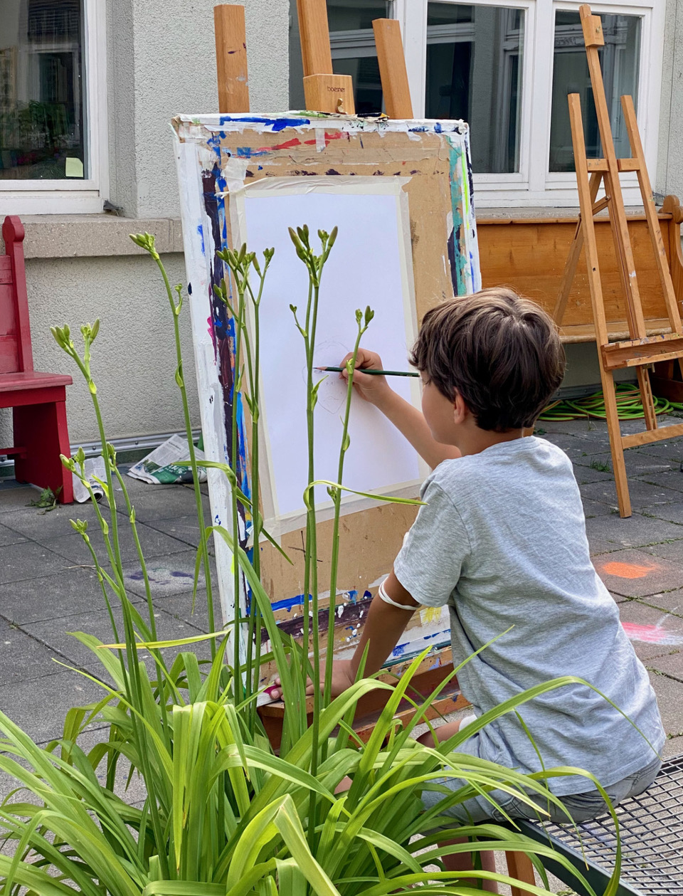 Junge sitzt vor einer Staffelei und zeichnet mit Bleistift