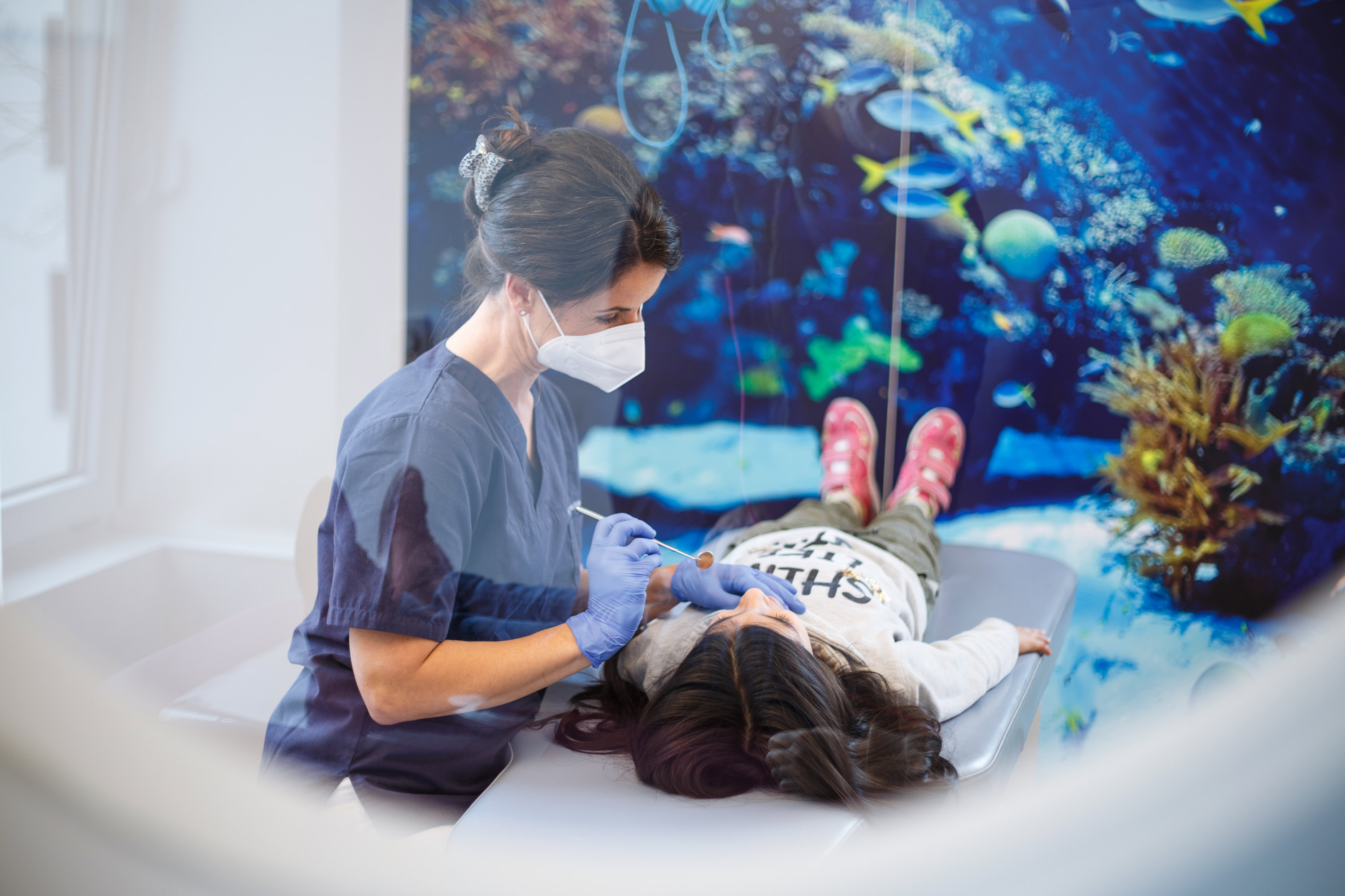 Zahnärztin mit medizinischem Spiegel in der Hand untersucht ein liegendes Kind