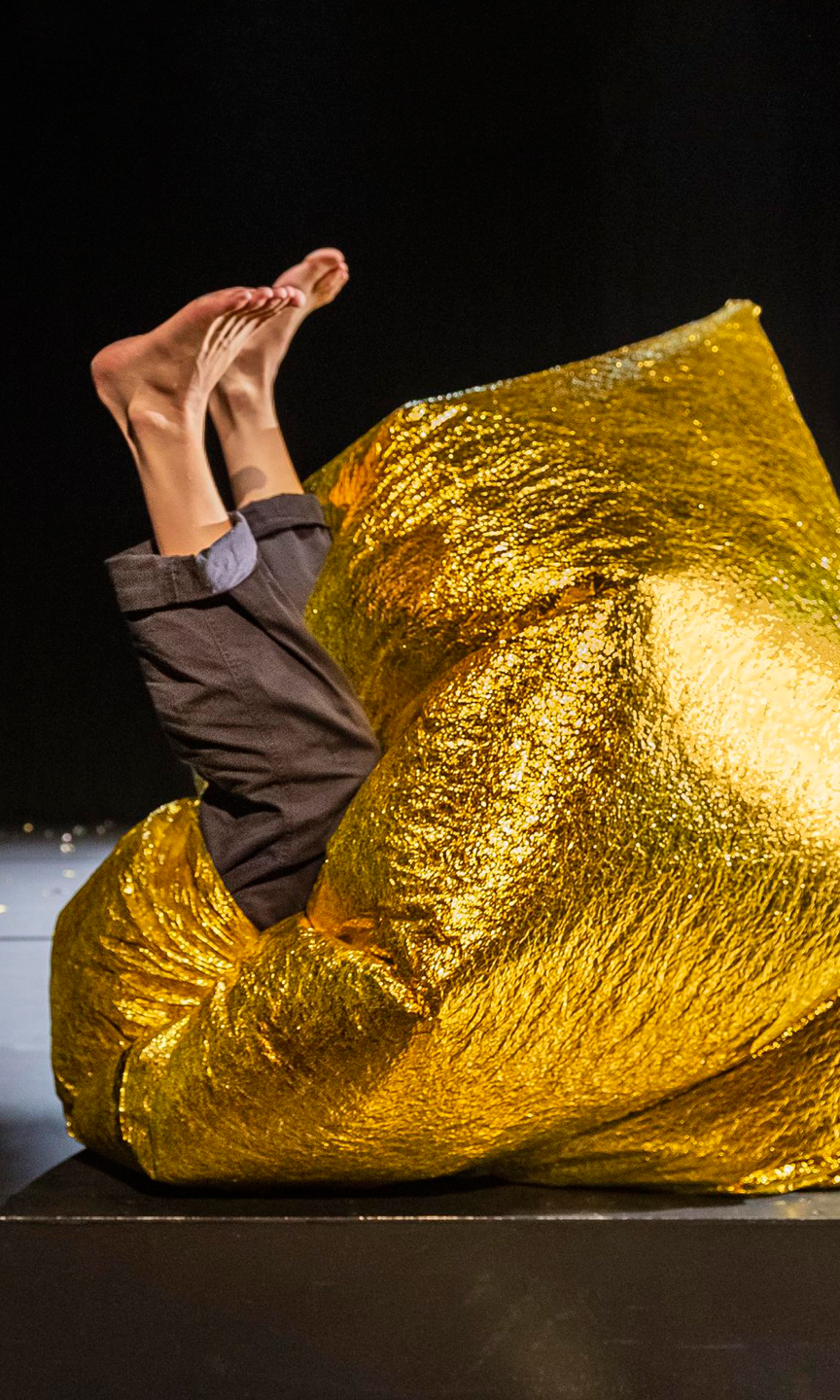 Menschliche Füße ragen aus einem großen Ball aus goldener Folie heraus.