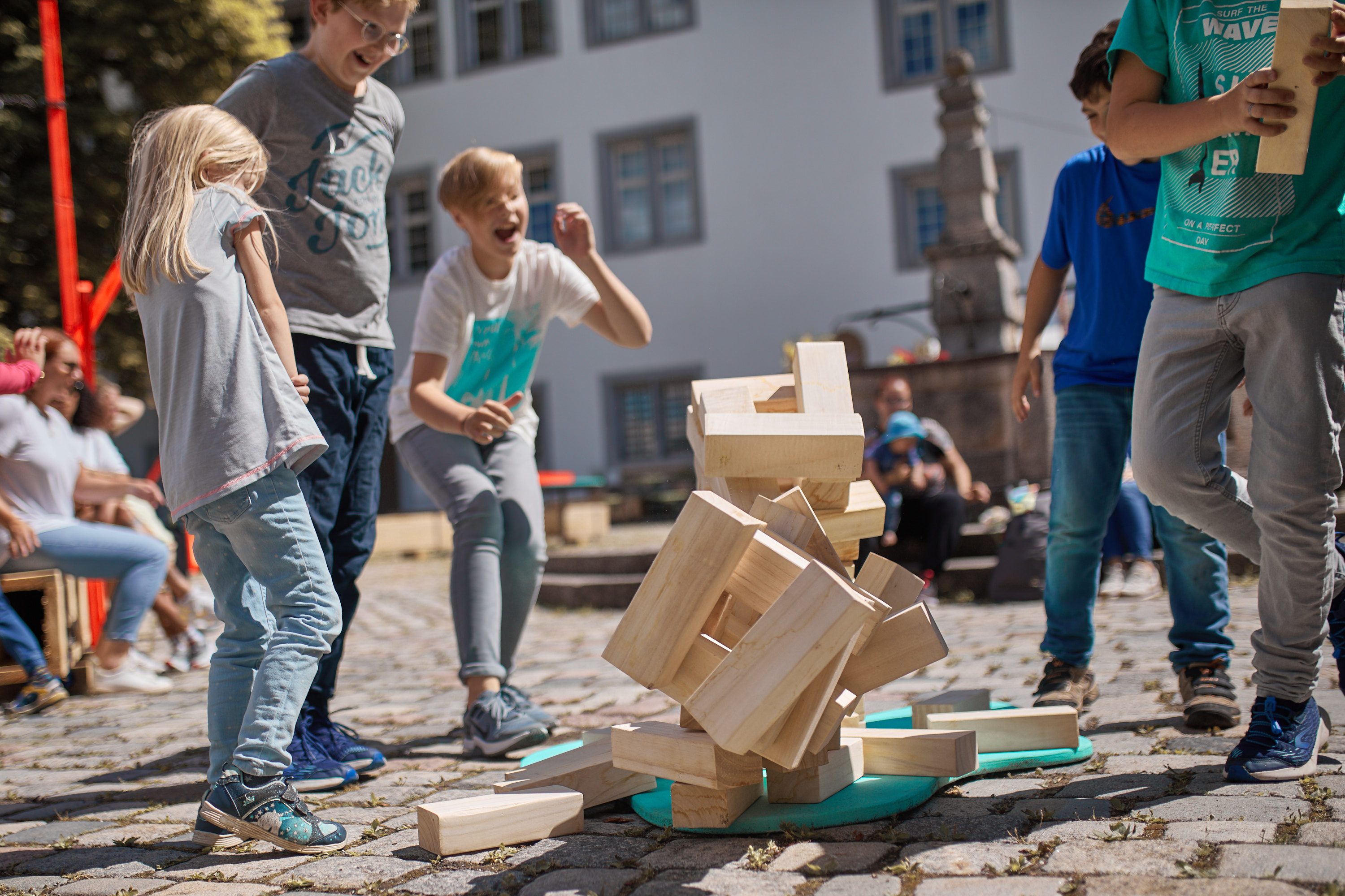Kinder um einen Holzstapelturm, der zusammenfällt