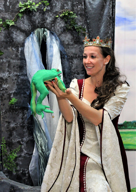 Dornröschen steht vor einem Schloss und schaut einen Frosch in ihren Händen an.