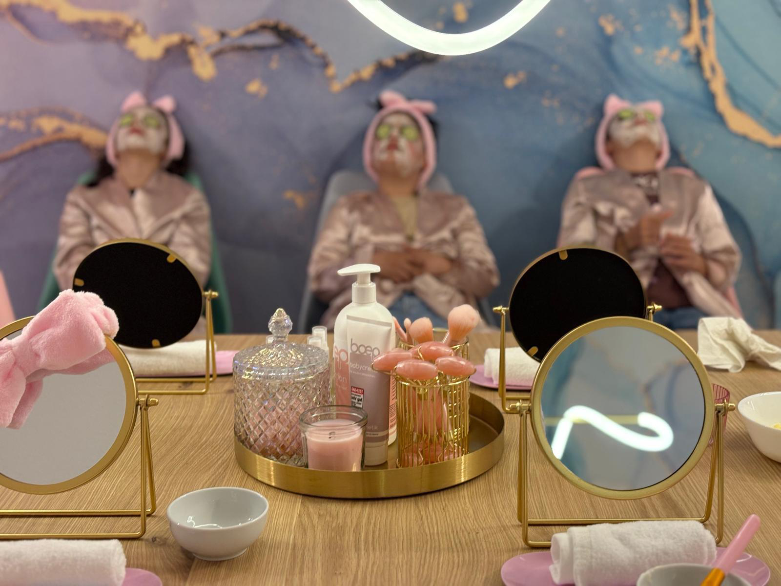 Drei Mädchen haben eine Gesichtsmaske auf dem Gesicht und sitzen vor Schminktischen.