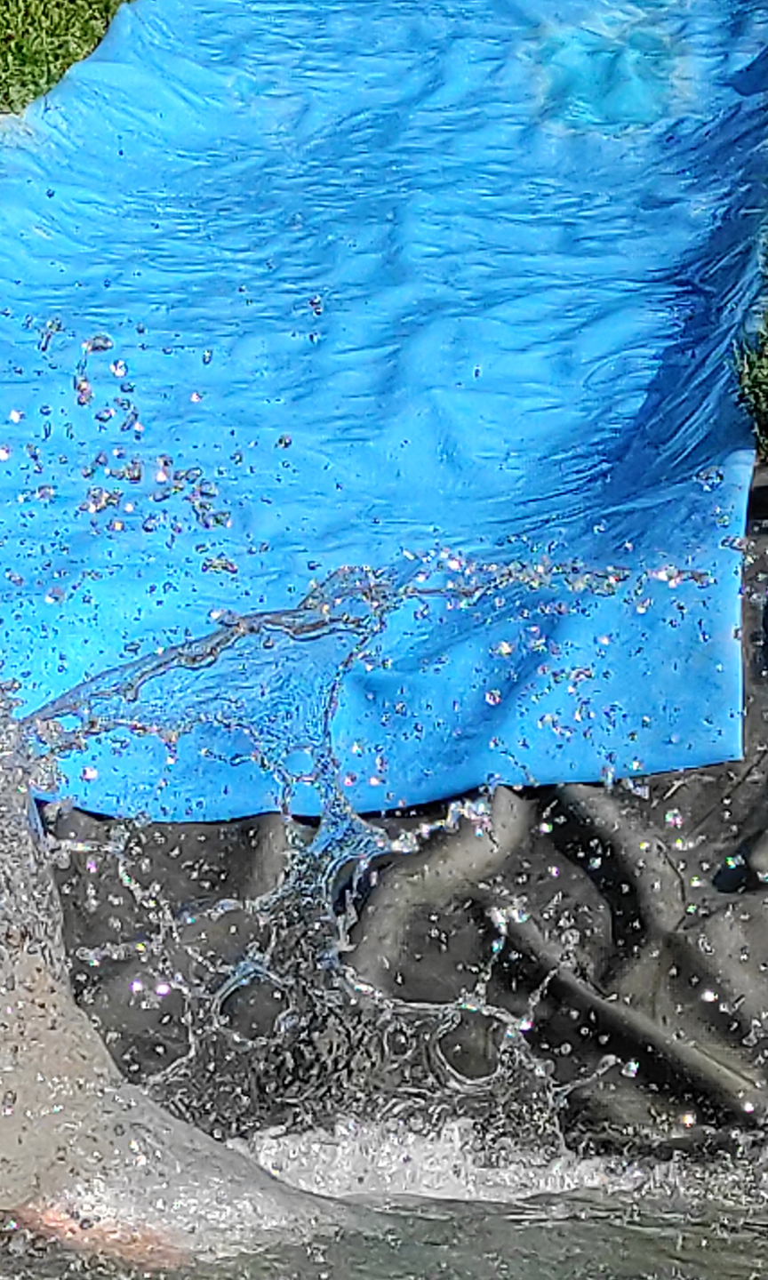 Eine Rutsche aus einem Stück Plastik führt in ein kleines Wasserbecken. Wassertropfen fliegen.