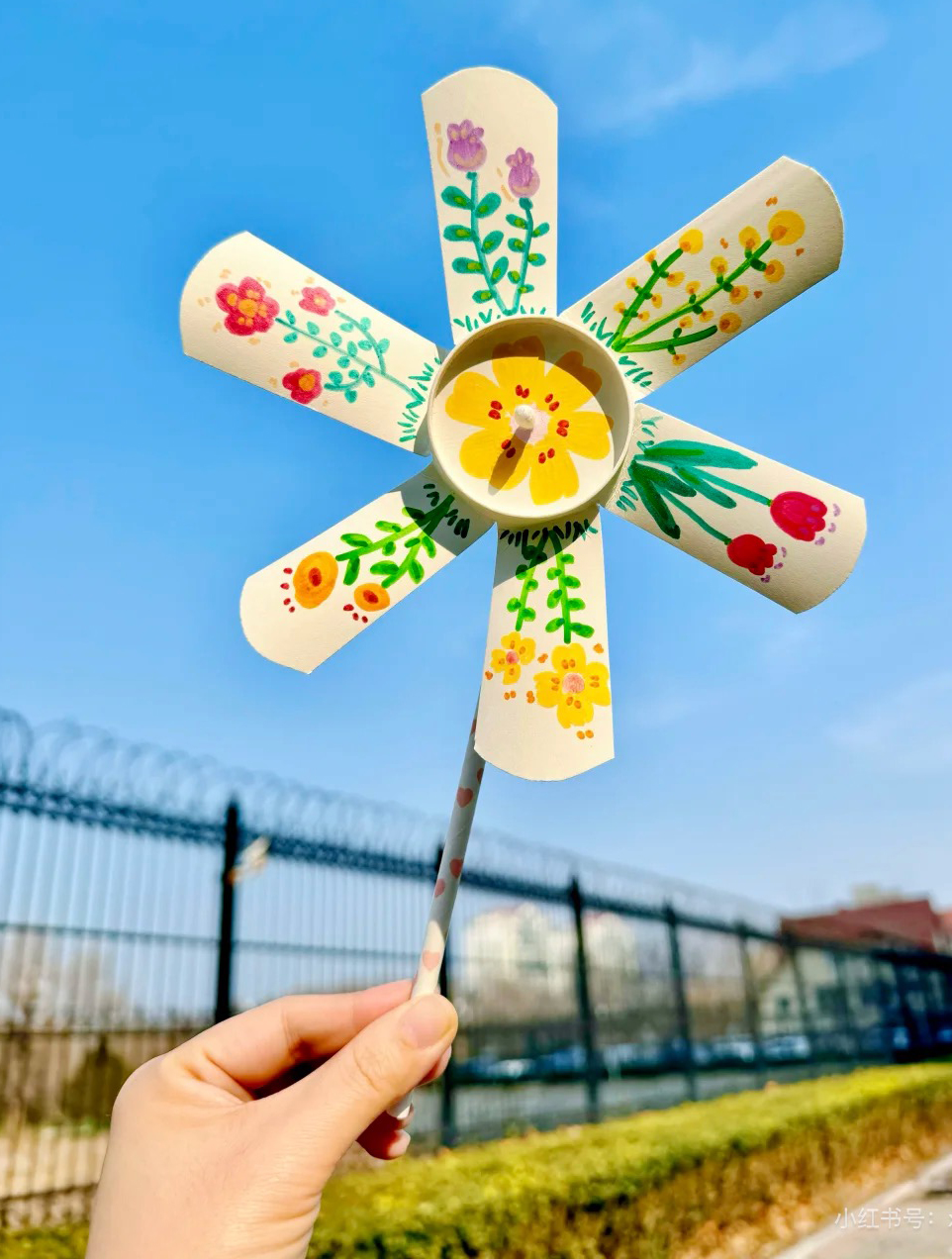 Eine Hand hält ein Windrad aus Papier in der Hand. Es ist bunt gemalt.